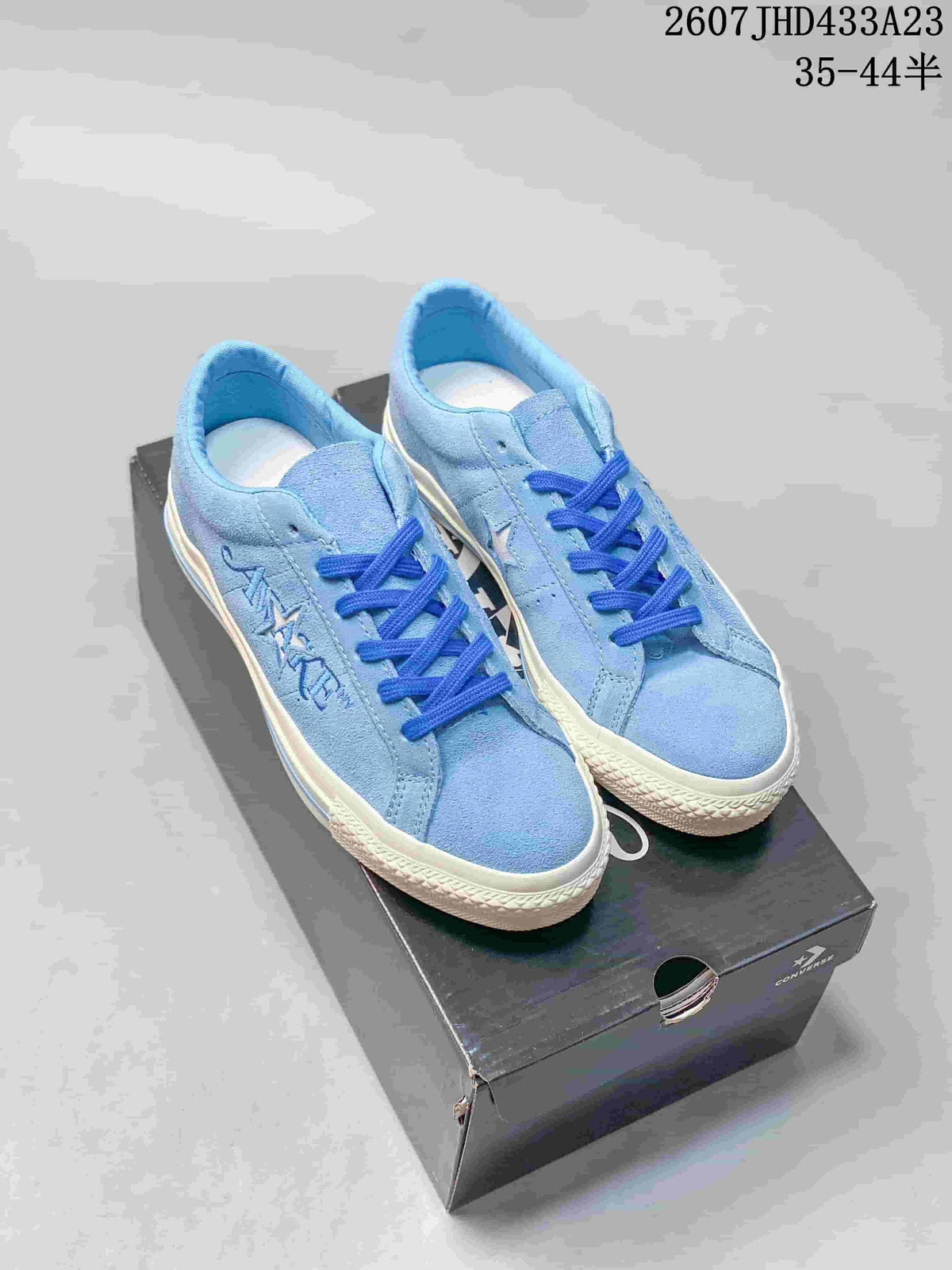 Pair of light blue Converse low-top sneakers with blue laces displayed on a shoebox; style code and size range text are visible above.
