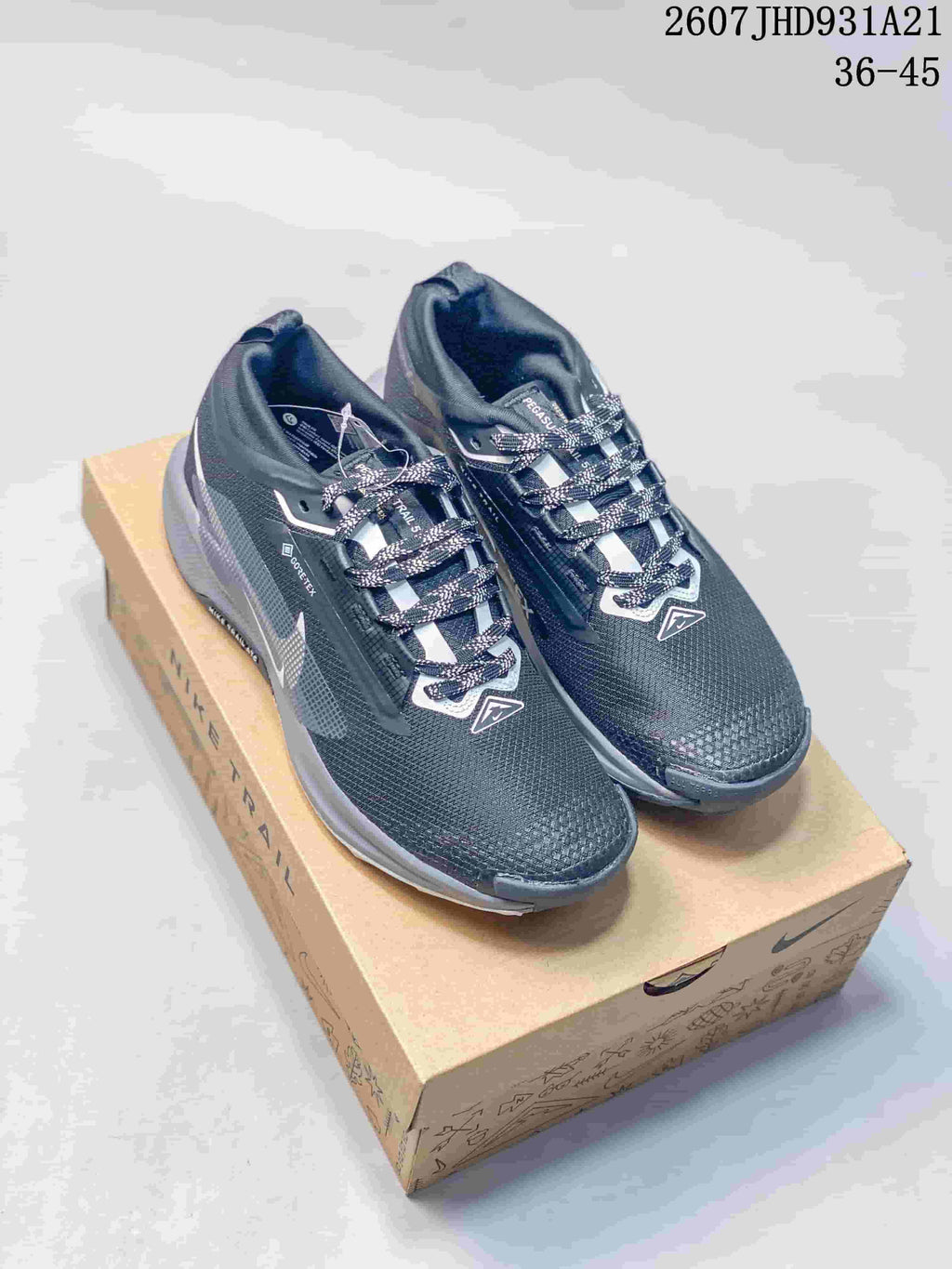 Pair of dark gray Nike trail sneakers displayed on a Nike shoe box, with white detailing and patterned laces.