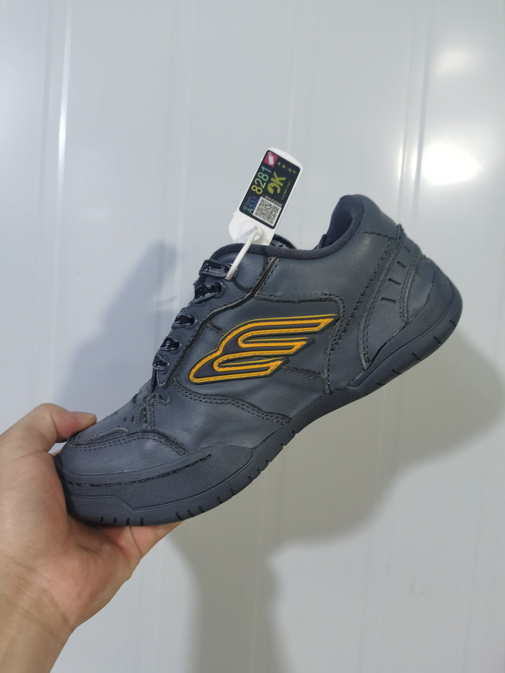 Close-up angled view of a dark grey Balenciaga Hampton sneaker with yellow side detailing and black laces.