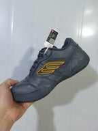 Close-up angled view of a dark grey Balenciaga Hampton sneaker with yellow side detailing and black laces.