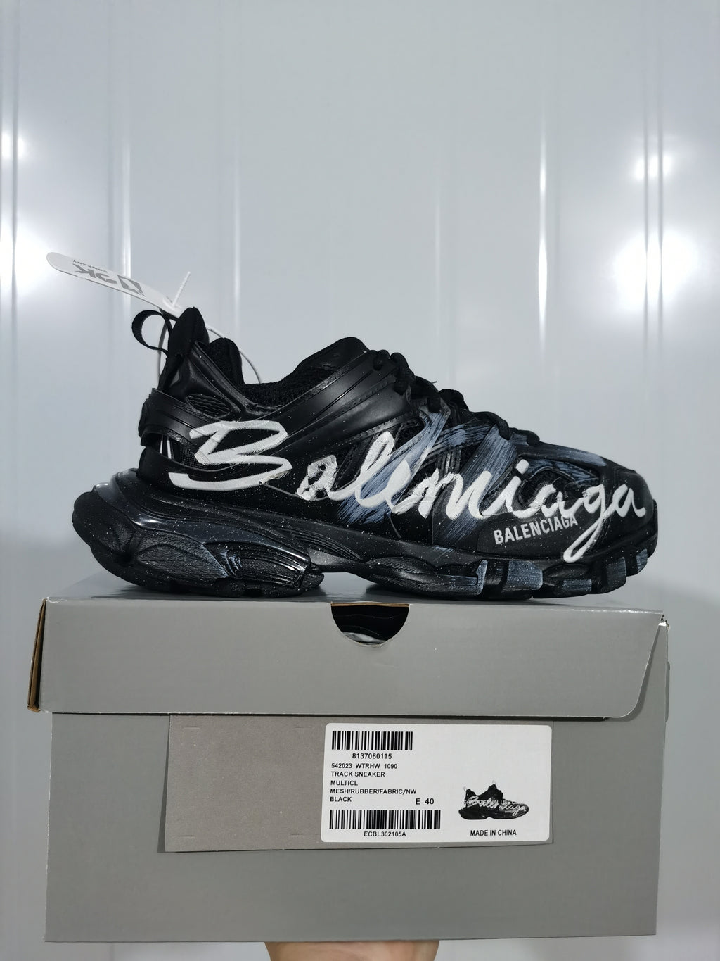 Side view of a black Balenciaga Track sneaker with white graffiti lettering displayed on its shoebox.