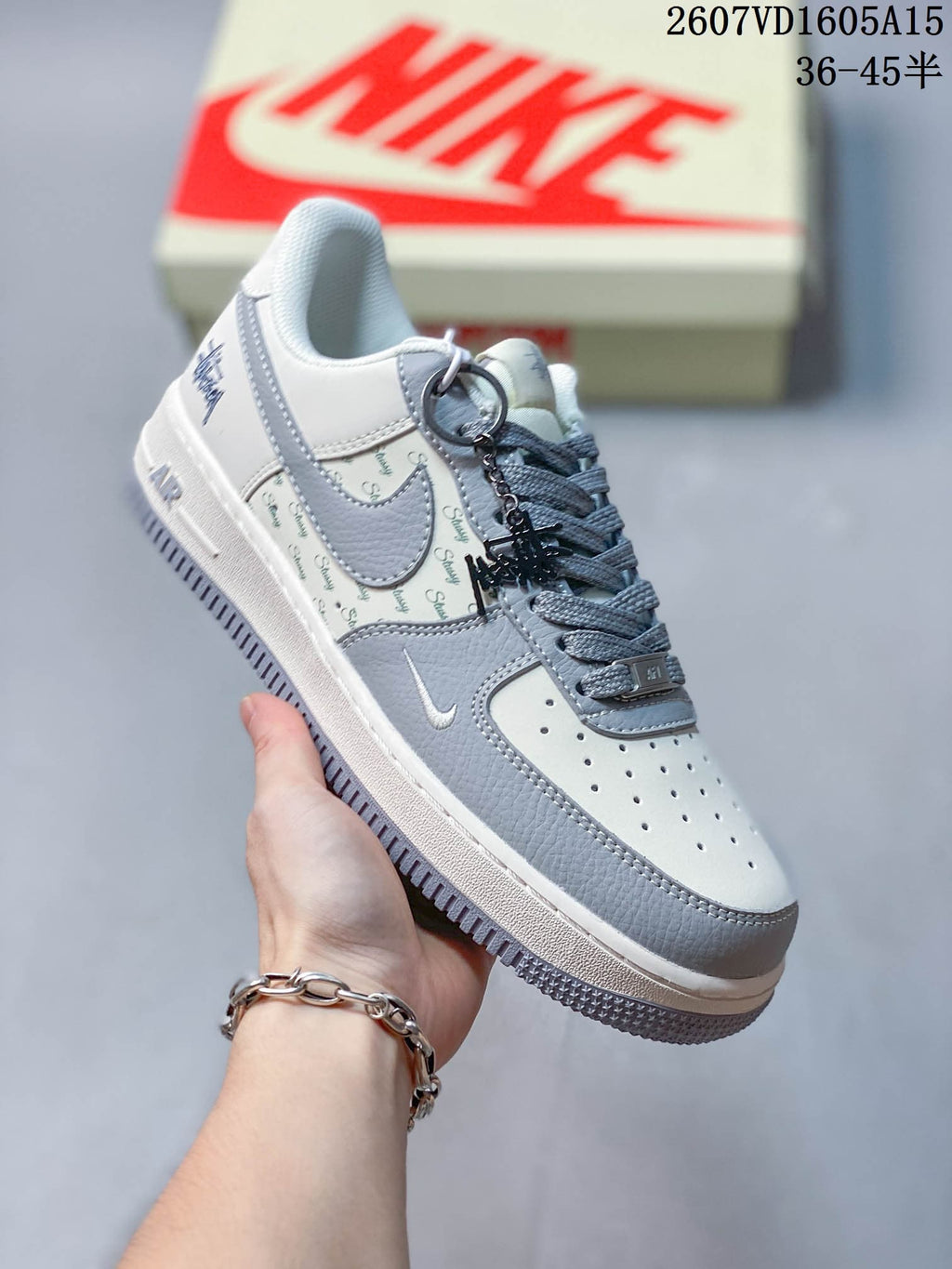 Three-quarter side view showing the patterned side panel, grey overlays, decorative metal charm, Nike Swoosh, and Air midsole detail.
