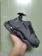 Close-up angled view of dark grey Balenciaga sneakers showing the layered upper, mesh panels, tonal stitching and chunky sculpted sole.