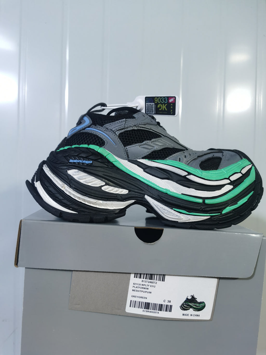 Grey, black and green New Balance sneaker displayed on its box, with the box label visible.