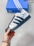 Side profile showing the white upper, black three-stripe detailing, shell toe, and dark outsole.