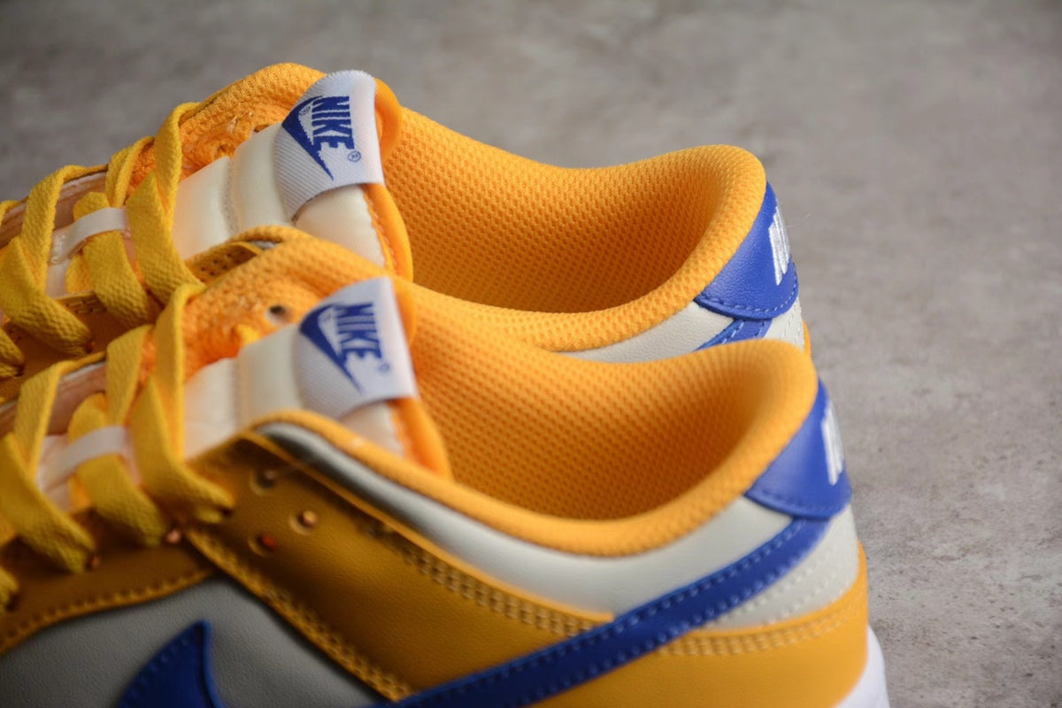 Close-up of the wheat gold and white Nike sneakers showing padded orange-gold collars, blue heel details, and tongue branding.