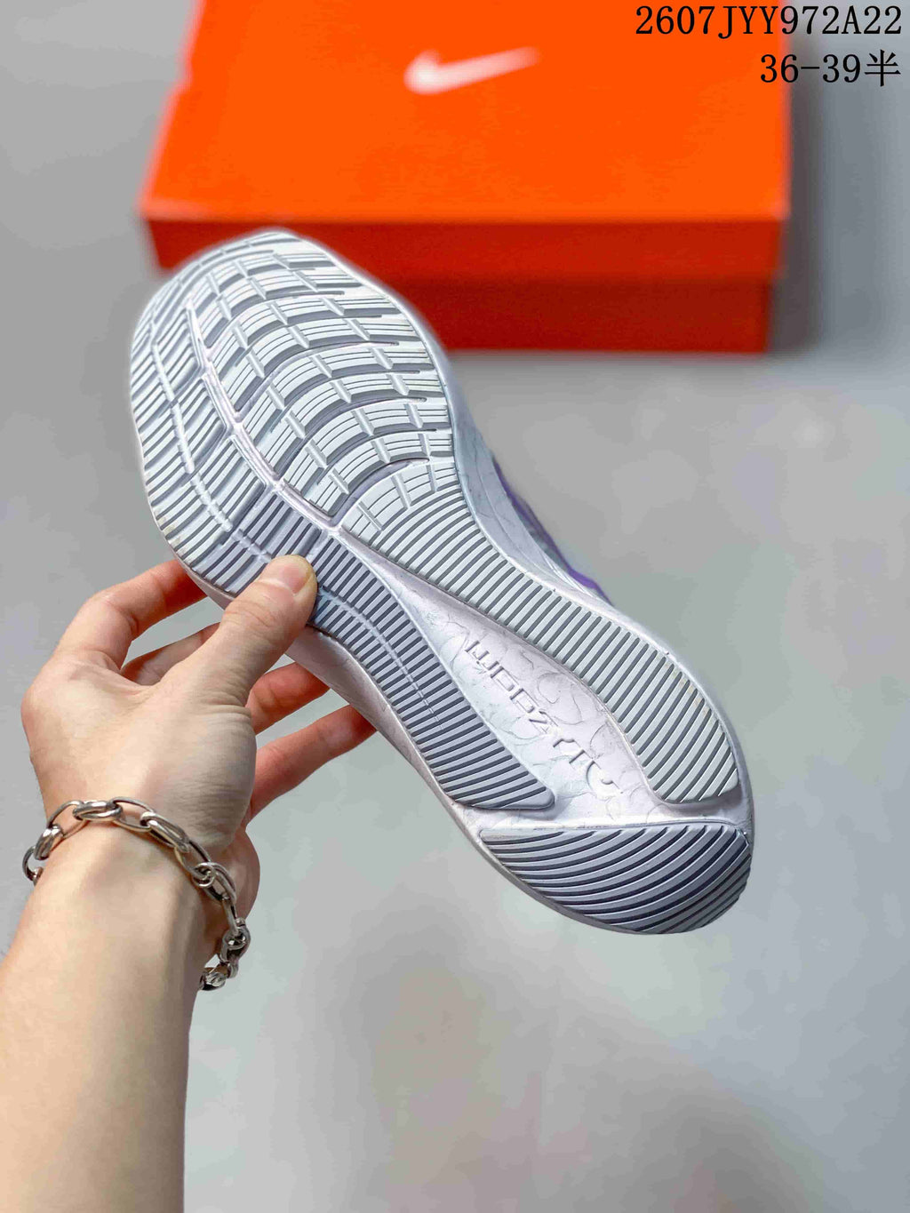 Close-up of the textured outsole of a light gray Nike running shoe, showing segmented tread and an orange shoebox in the background.