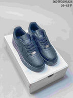Pair of black low-top sneakers displayed on a shoebox, showing perforated toe boxes, tonal branding, and metal lace tags.