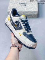 Angled side view of a white, navy, and yellow Nike Air Force 1 sneaker showing the layered side branding, yellow accent, and dark outsole.