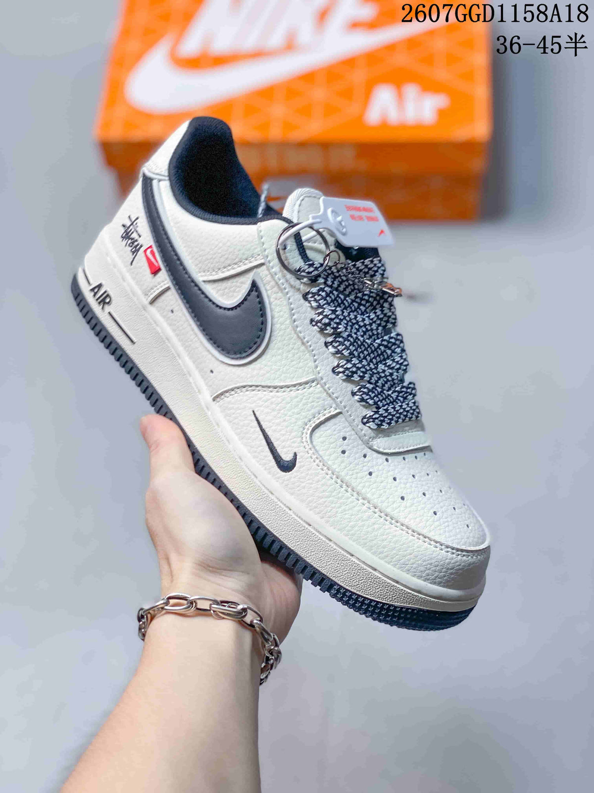 Close-up side view of a white sneaker with a dark swoosh, patterned laces, decorative side branding, and a dark outsole.