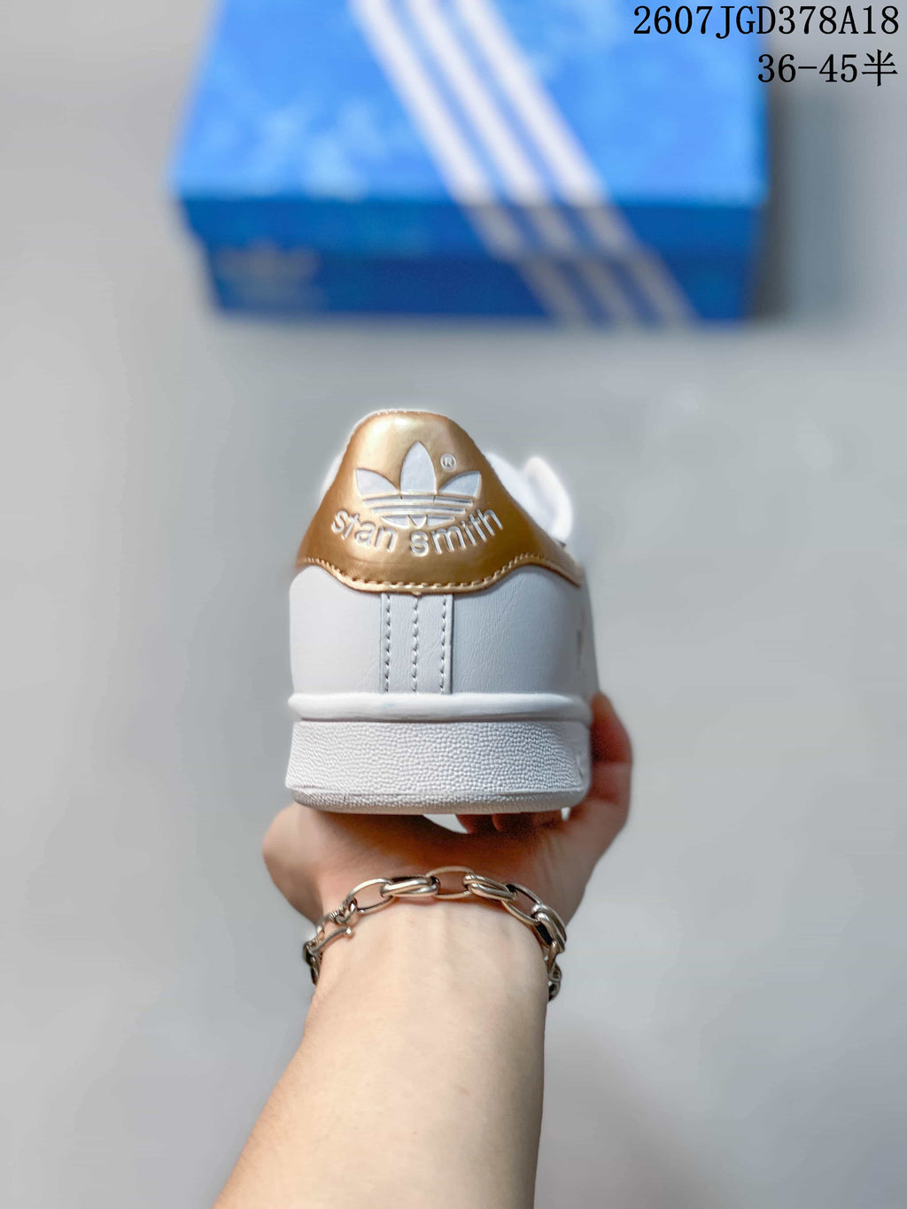 Rear view of a white Stan Smith sneaker with a gold heel tab and embossed branding.