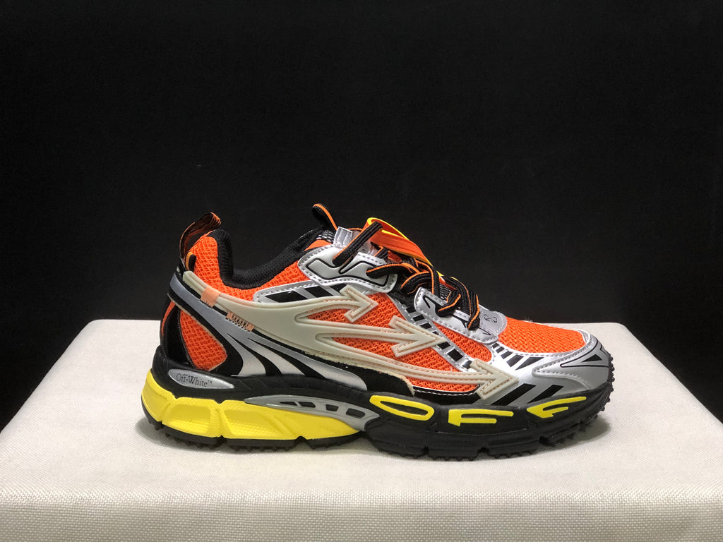 Close side profile showing the orange upper, silver toe overlay, black graphic details, and yellow outsole.