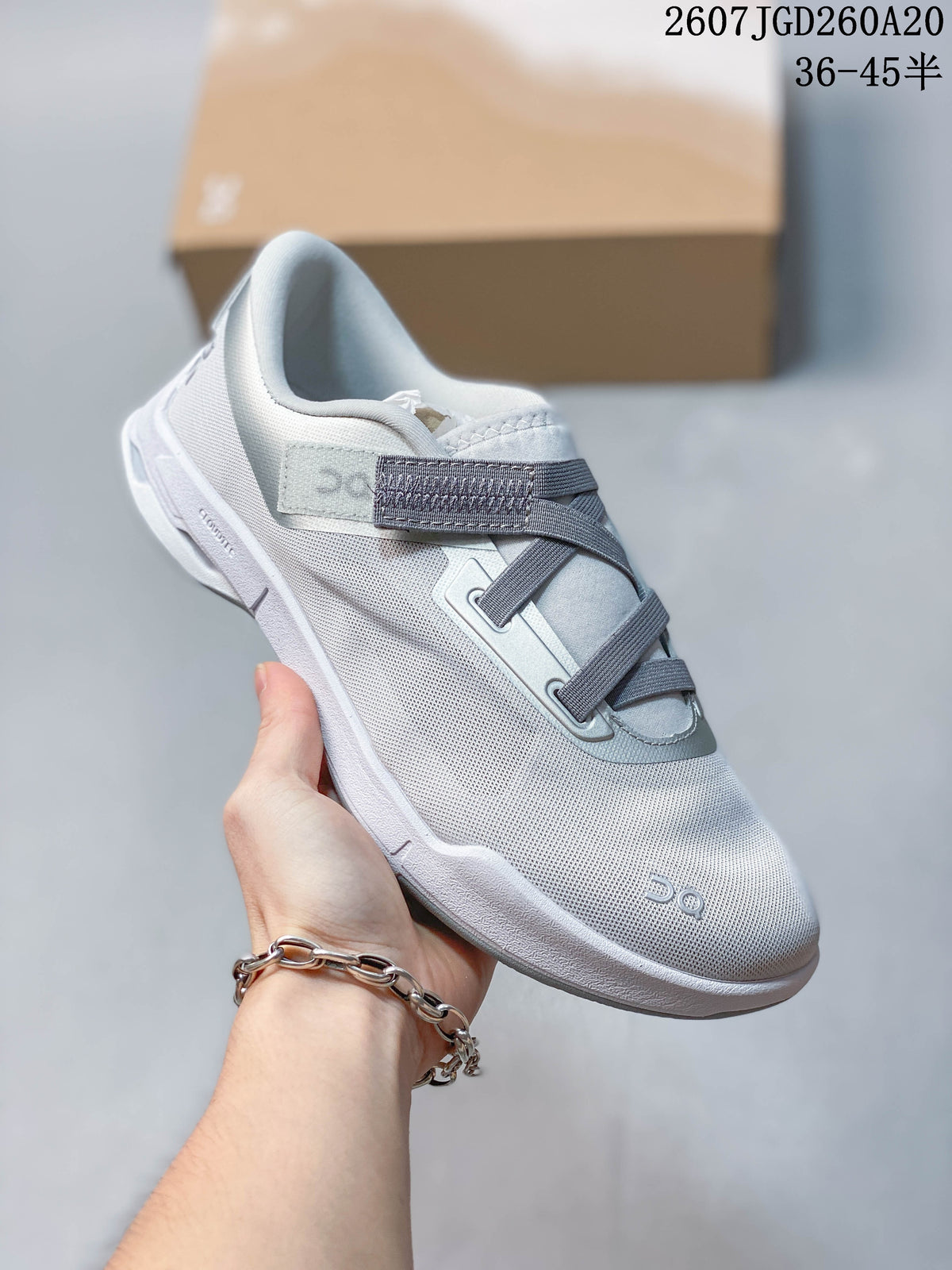 Angled side view of the light gray and white sneaker showing the breathable-looking textured upper, strap system, and raised sole.