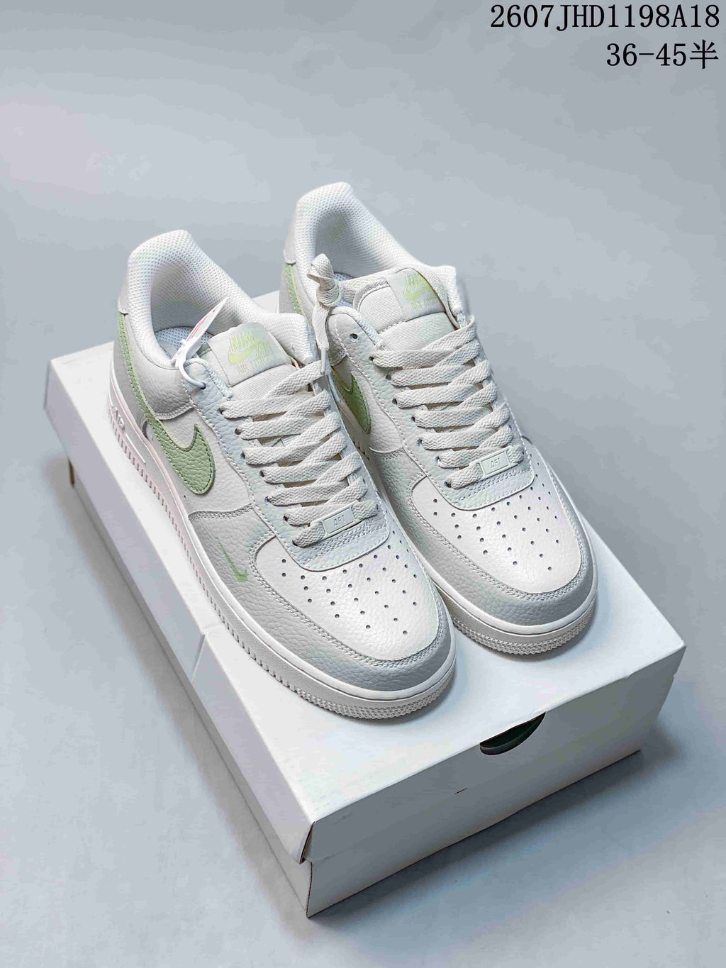 Pair of white low-top Nike Air Force 1 sneakers with light green accents displayed on a shoebox; image text shows style code 2607JHD1198A18 and size range 36–45.