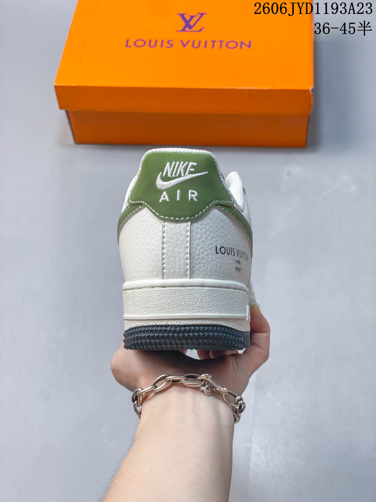 Rear view of a white sneaker with a green heel tab and branded detailing.