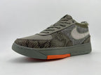 Angled view of gray Nike low-top sneakers with patterned overlays and an orange outsole accent