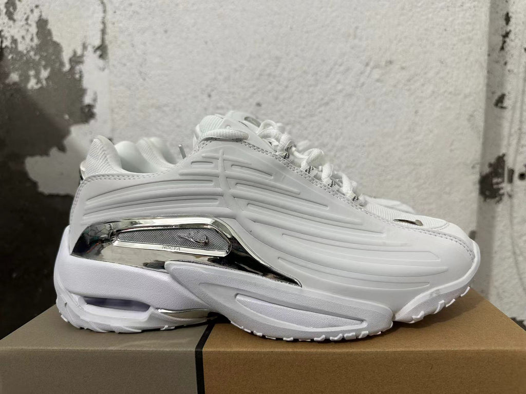 Side profile of a white Nike NOCTA Glide sneaker with sculpted panels and a silver-tone heel accent.