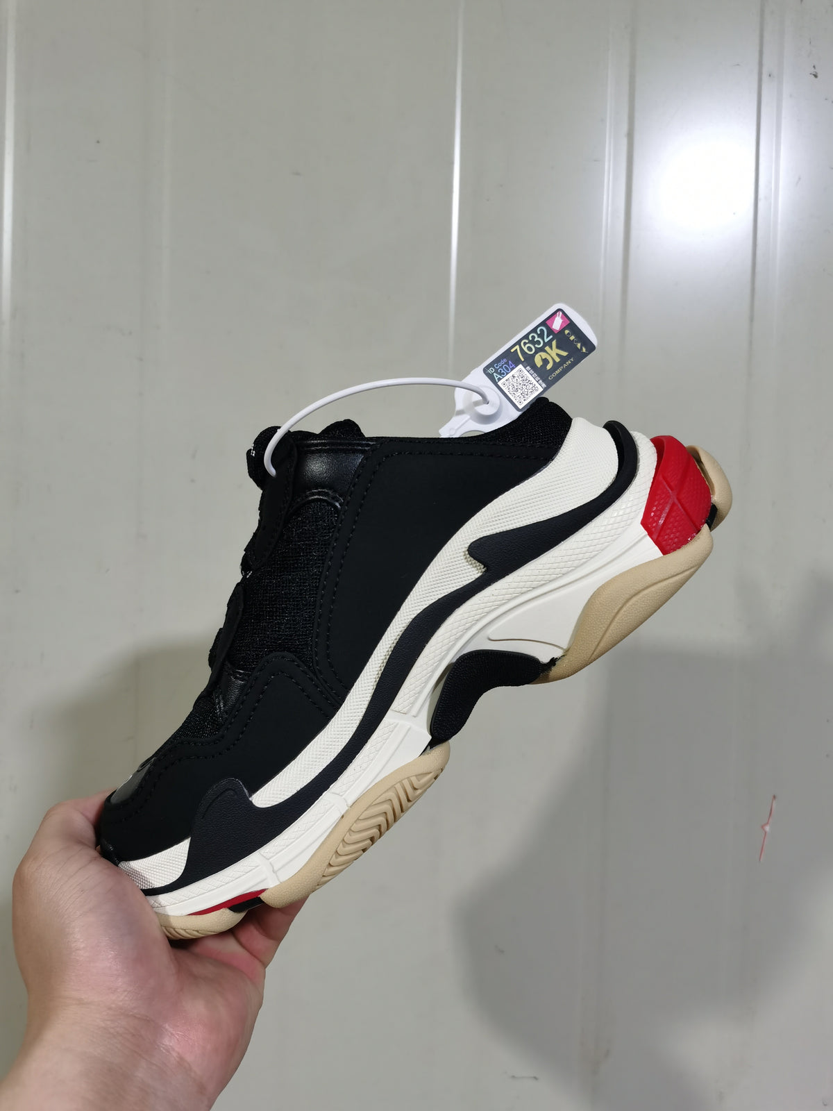 Side view of a black and white Balenciaga sneaker with red and beige sole accents, held against a light background.
