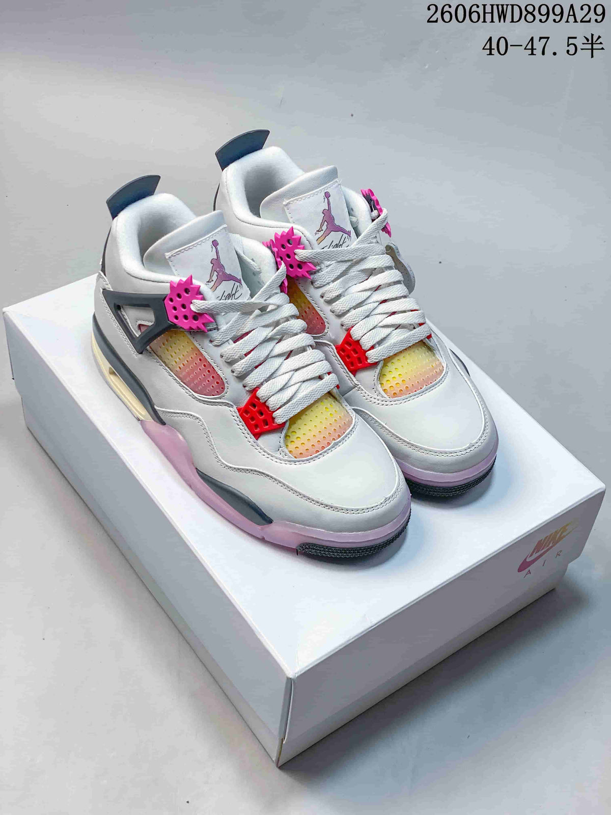 Pair of white and gray Jordan 4-style sneakers with bright pink details and gradient panels, shown from the front.