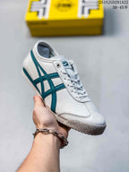 White Onitsuka Tiger sneaker held in hand, showing teal contrast stripes and a textured outsole.