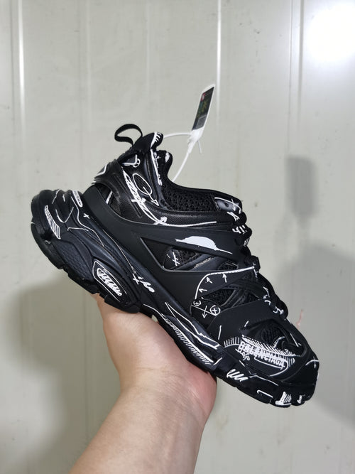 Angled close-up of the black and white track sneaker showing the open side panels, lace-up front, padded collar, and graphic overlays.
