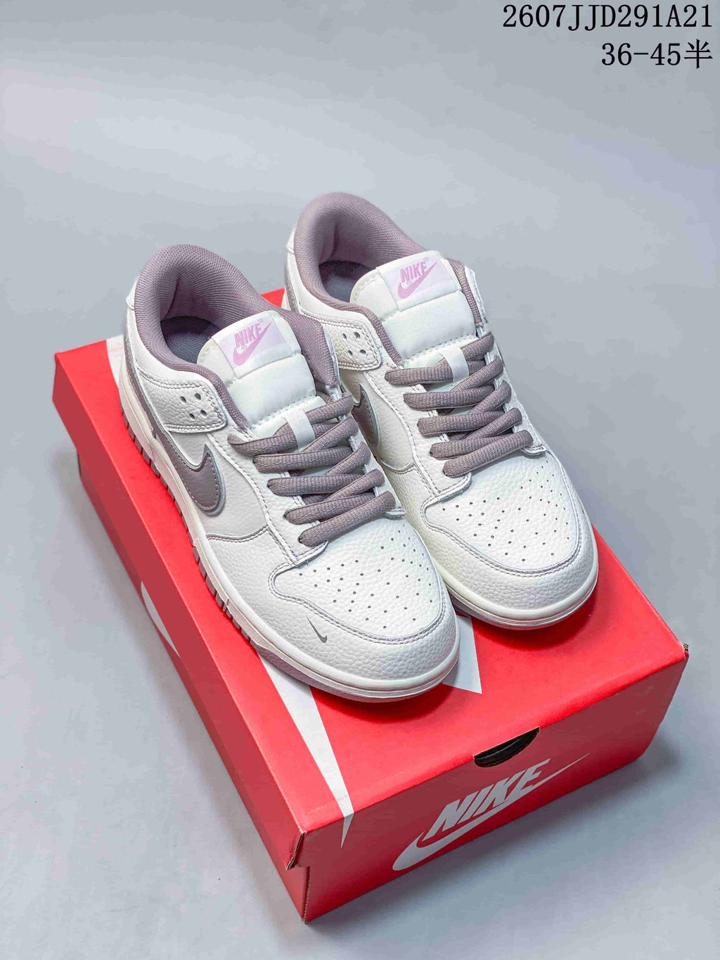 Pair of white and gray Nike sneakers displayed on a red shoebox, showing perforated toe boxes, gray laces, and padded collars.