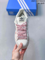 Top view showing the trefoil tongue label, ruffled pink laces, and textured shell toe.