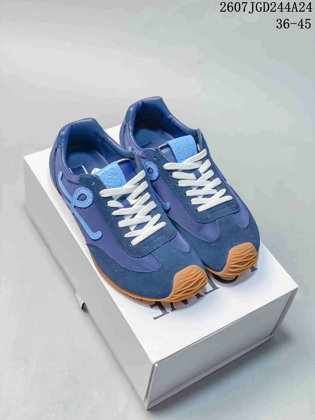 Pair of blue Loewe low-top sneakers displayed on a shoebox, showing white laces, light-blue side details, and gum-colored toe sections.