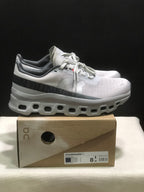 Side view of the On Cloudmonster 1 pair showing the dark heel band, lace-up upper, and cutout-style white outsole.