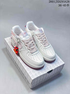 Pair of white and pale pink low-top sneakers displayed on a patterned shoe box, with a burgundy outsole and decorative charms.