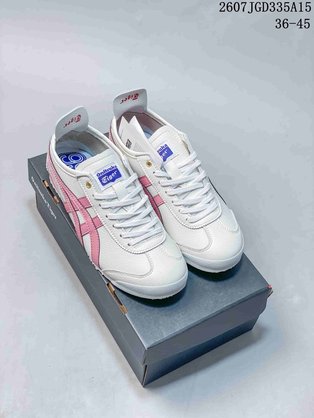 Pair of white and pink Onitsuka Tiger Mexico 66 Deluxe sneakers displayed on a branded shoe box; image text shows style code 2607JGD335A15 and size range 36–45.
