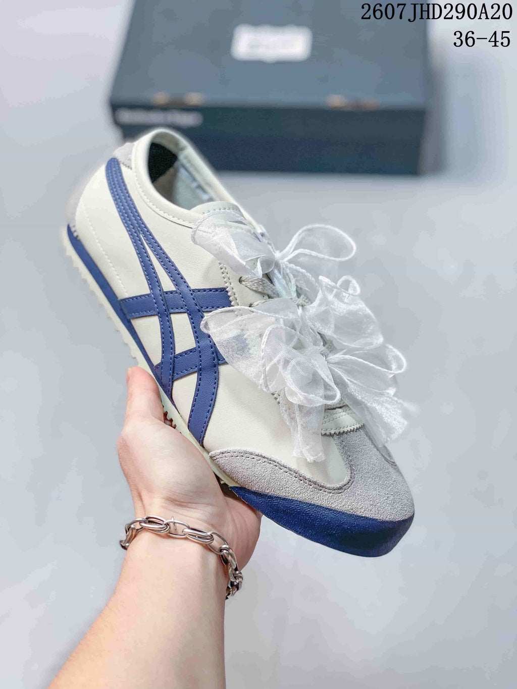 Angled view of a white sneaker with blue side stripes, gray toe detailing, and ribbon laces.