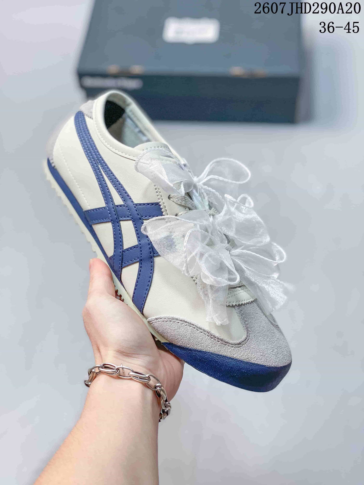 Angled view of a white sneaker with blue side stripes, gray toe detailing, and ribbon laces.