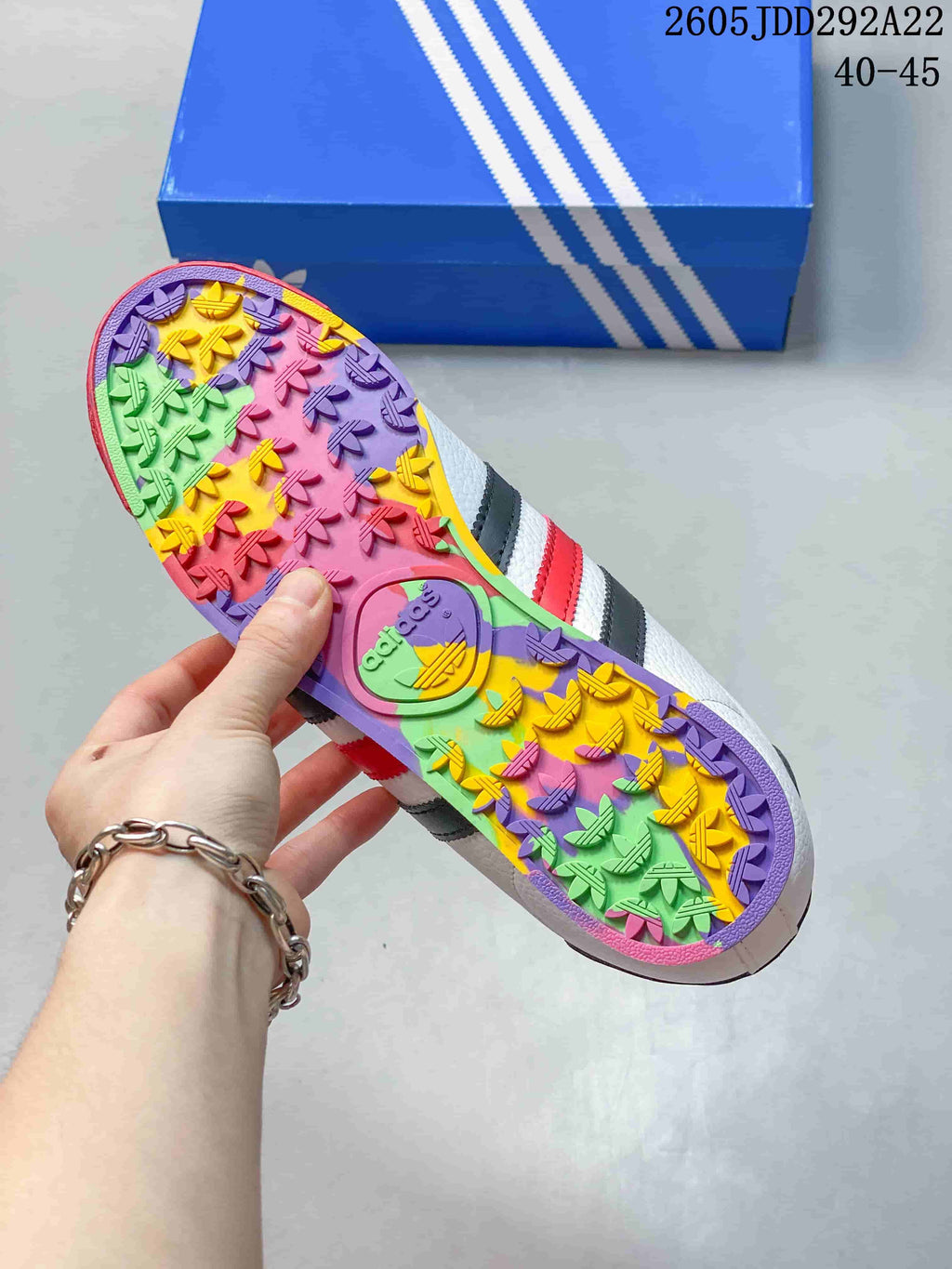 Outsole view showing the multicolor patterned sole of the adidas Samoa sneaker and a blue shoebox.