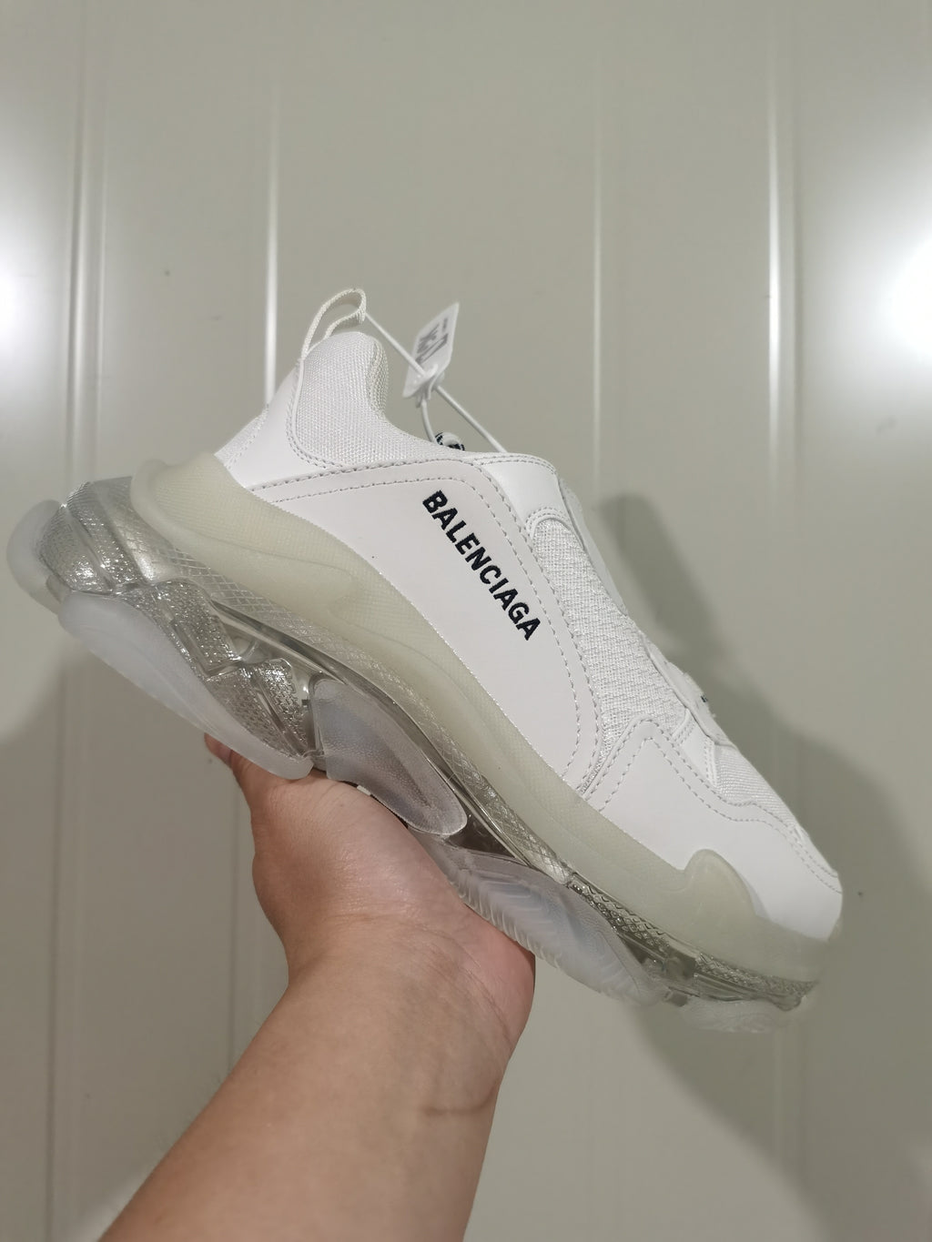 Side view of a white Balenciaga sneaker showing layered panels, black side lettering, a padded tongue, and a translucent sculpted sole.