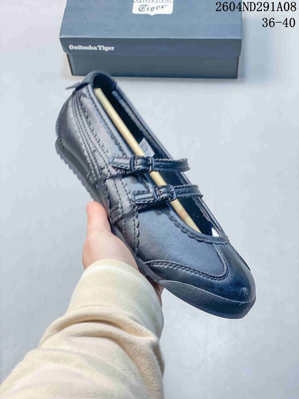 Angled close-up of the black Onitsuka Tiger sneaker showing its buckle straps, stitched side panels, and low-profile sole.