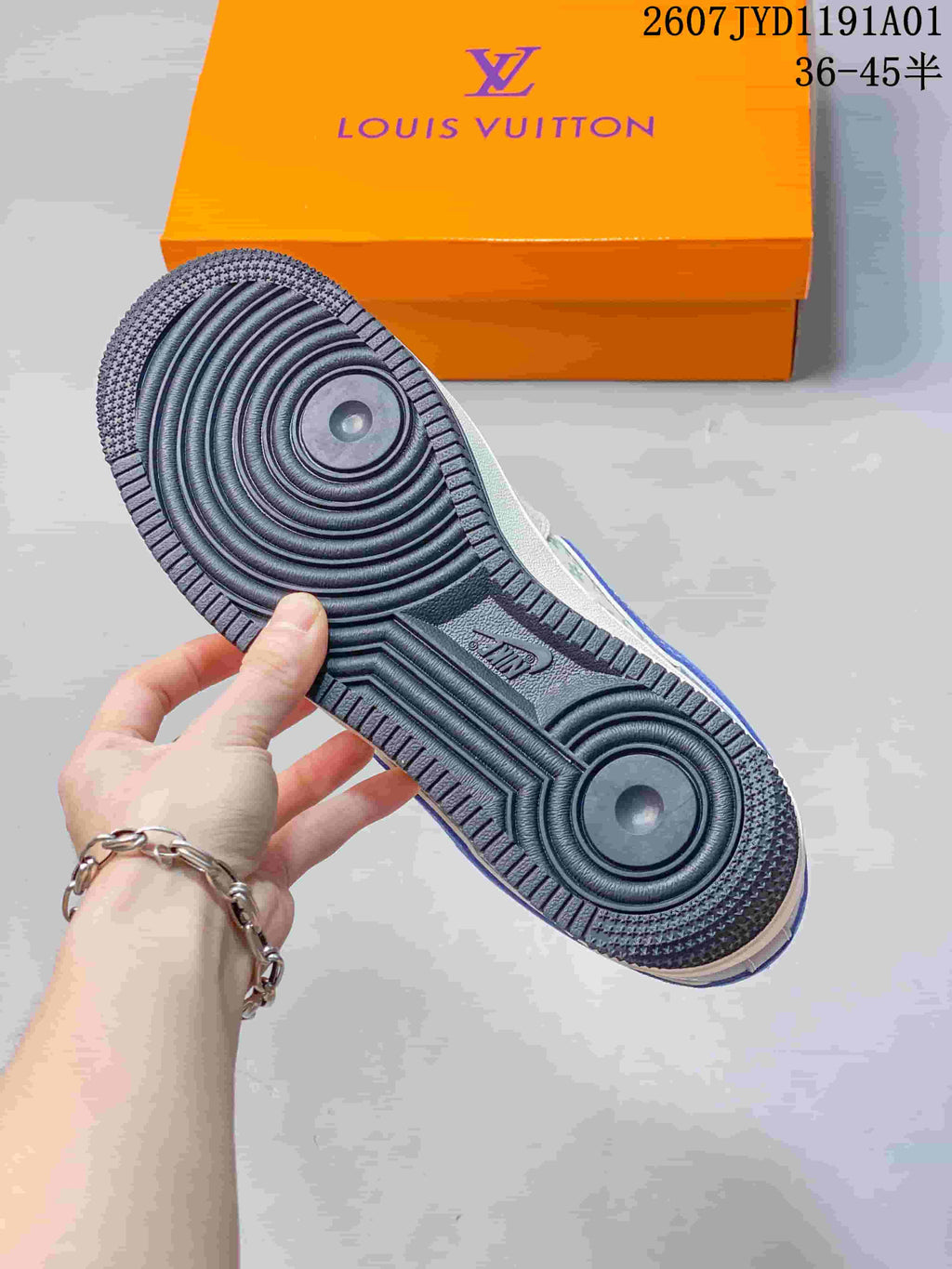 Underside view showing the dark outsole with circular tread and an orange shoe box.