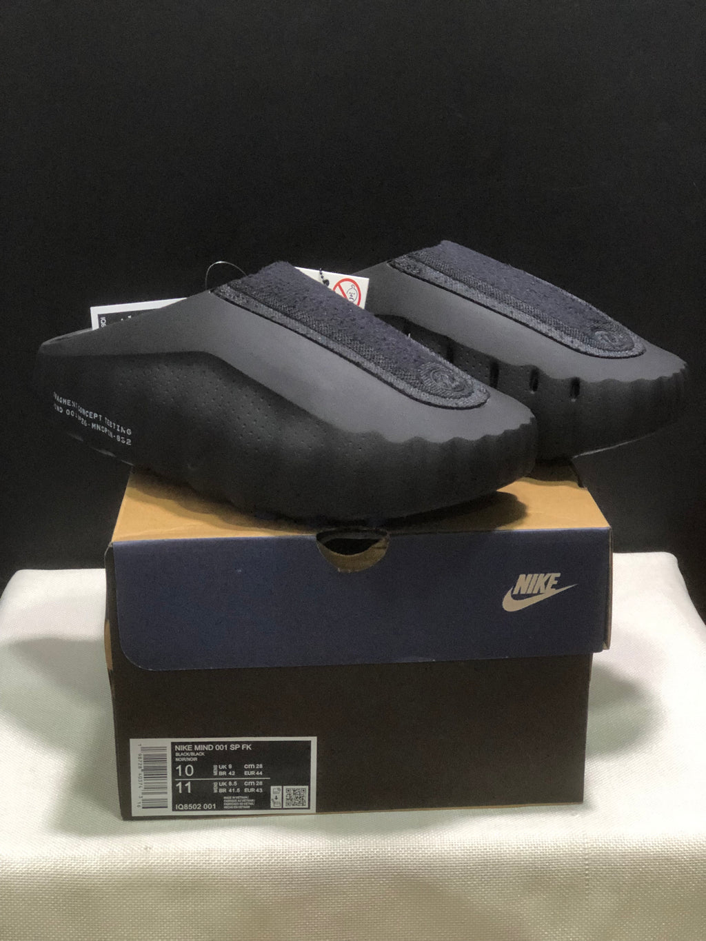 Black Nike Mind 001 slides displayed on a Nike shoebox, showing the closed-toe shape and textured upper panels.
