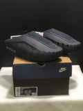Black Nike Mind 001 slides displayed on a Nike shoebox, showing the closed-toe shape and textured upper panels.