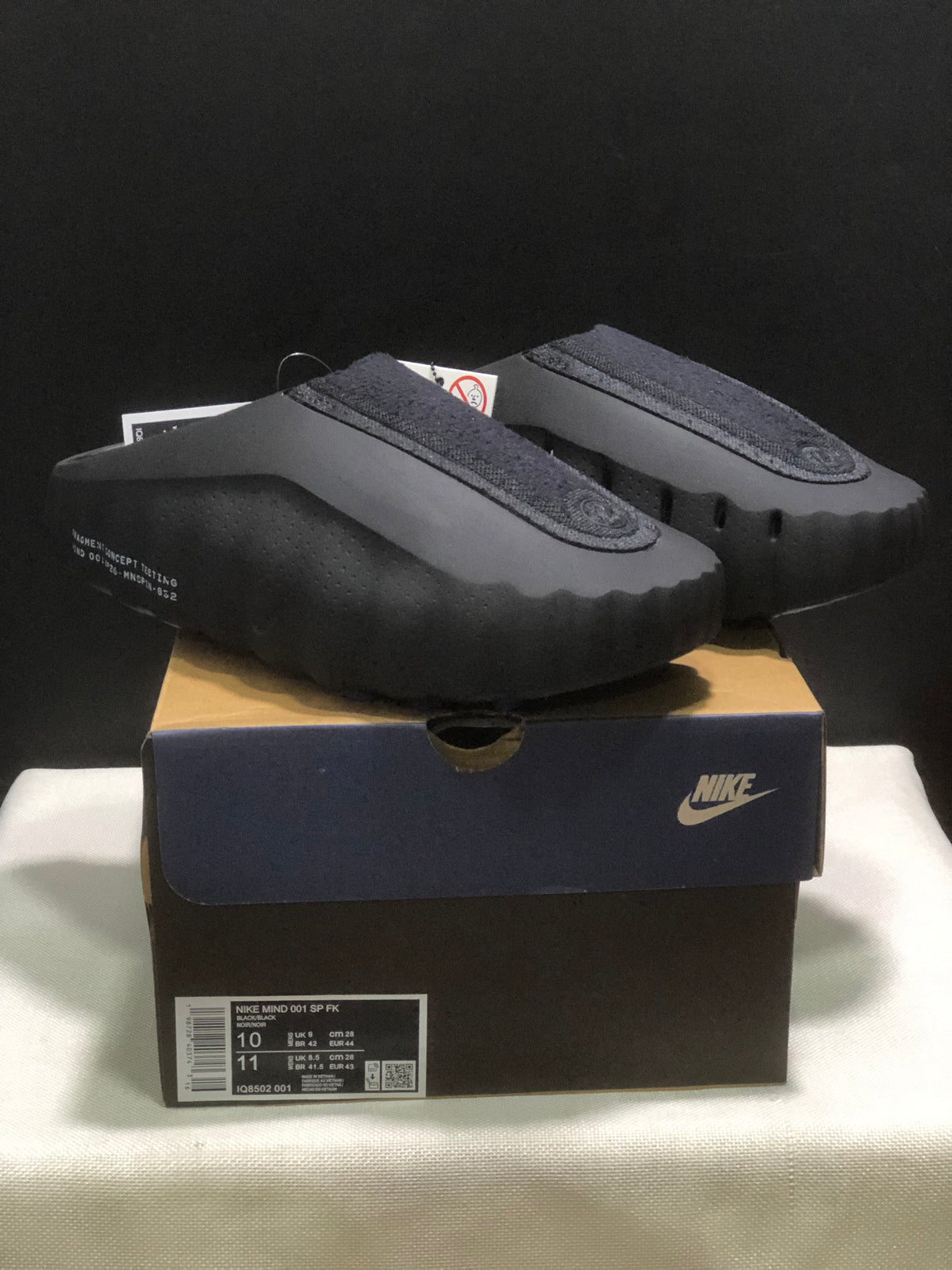 Black Nike Mind 001 slides displayed on a Nike shoebox, showing the closed-toe shape and textured upper panels.