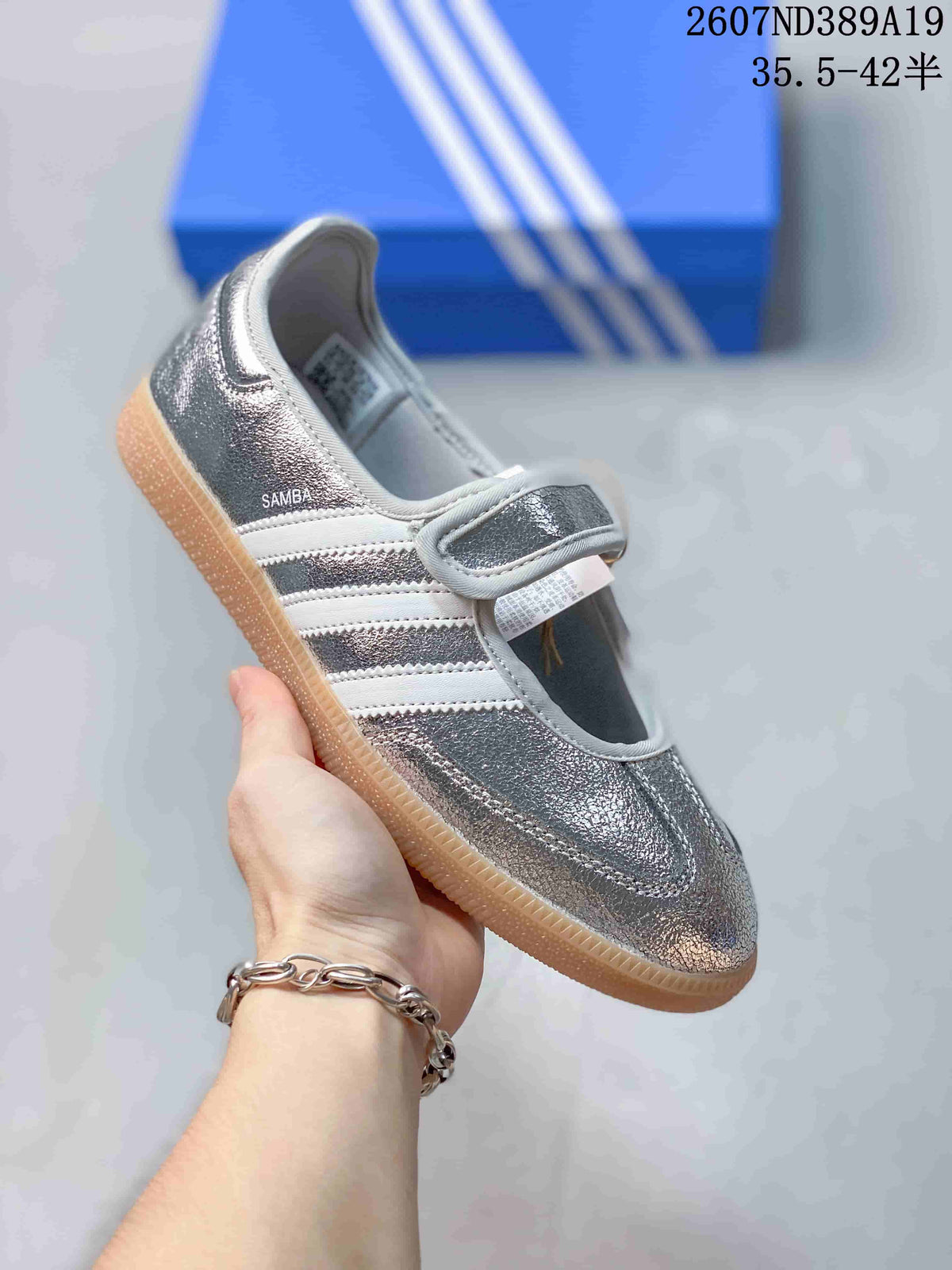Side view of a metallic silver Samba Jane sneaker showing the adjustable strap, three stripes, and gum-colored outsole.