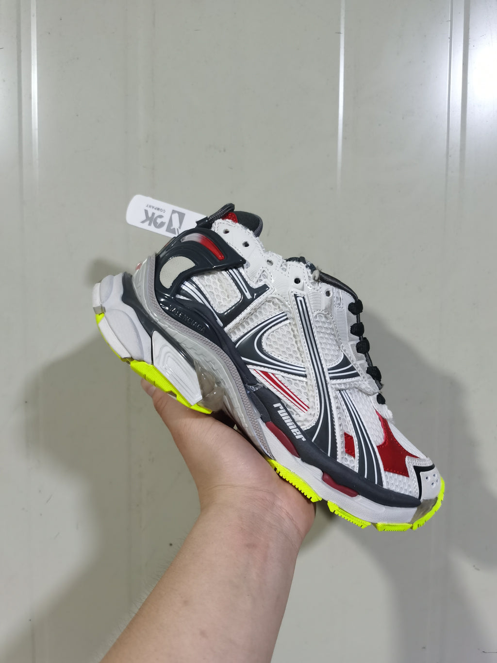Close angled view of the Balenciaga Runner sneaker showing layered panels, mesh-style sections, black laces and contrasting red details.