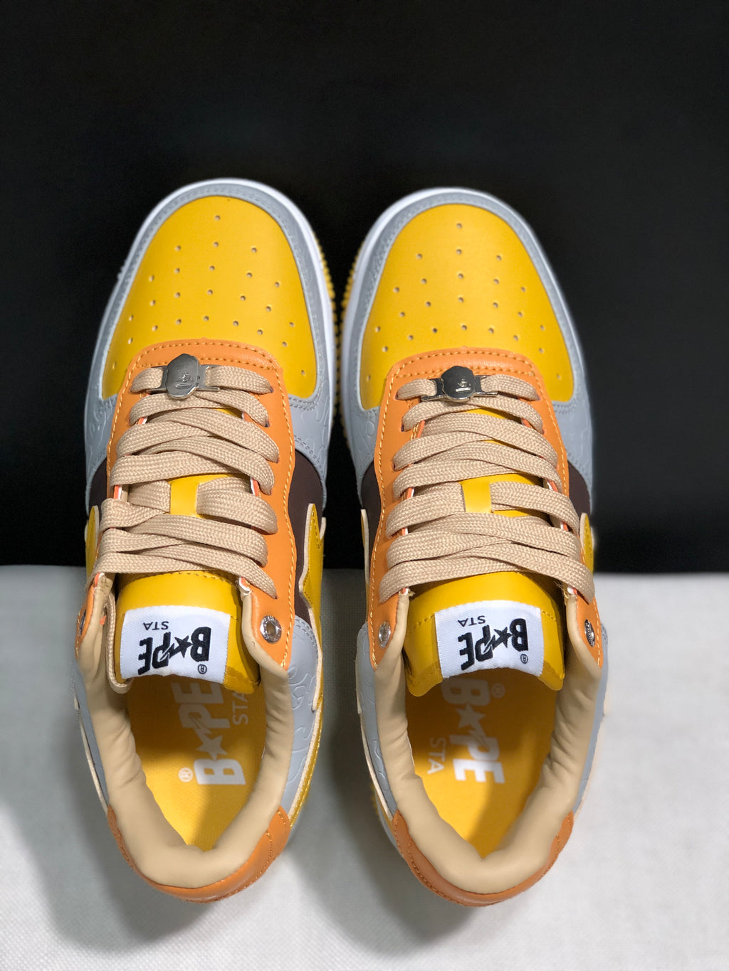 Top-down view of the pair showing yellow perforated toe boxes, beige laces, and orange eyestay panels.
