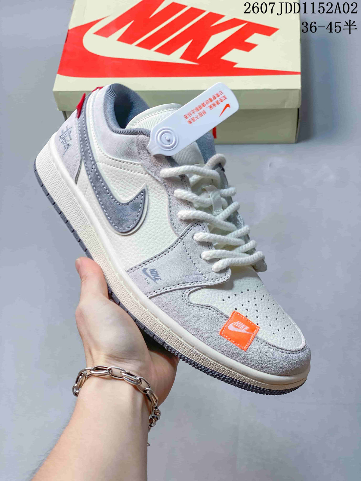 Angled side view of the white and light gray low-top sneaker with gray Swoosh and orange forefoot detail.