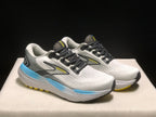Three-quarter view of the Brooks Glycerin 21 pair, showing the white and grey uppers, black laces, Brooks side branding, and blue sole accents.
