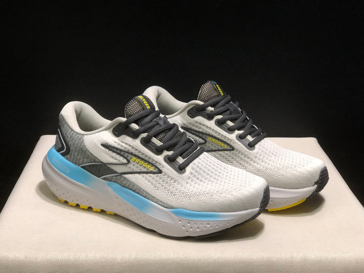 Three-quarter view of the Brooks Glycerin 21 pair, showing the white and grey uppers, black laces, Brooks side branding, and blue sole accents.