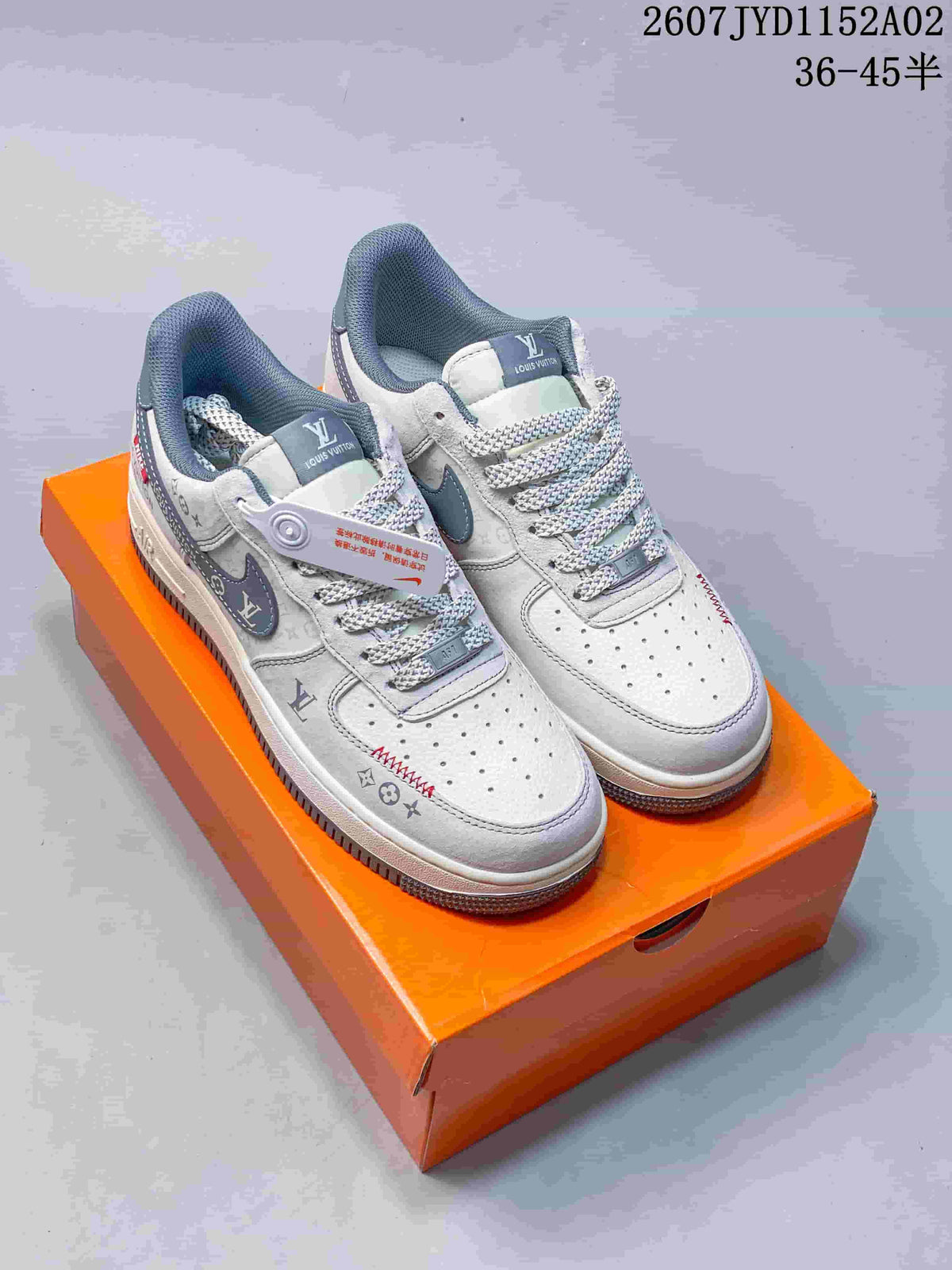 Light gray low-top sneakers with patterned panels and laces, shown on an orange box