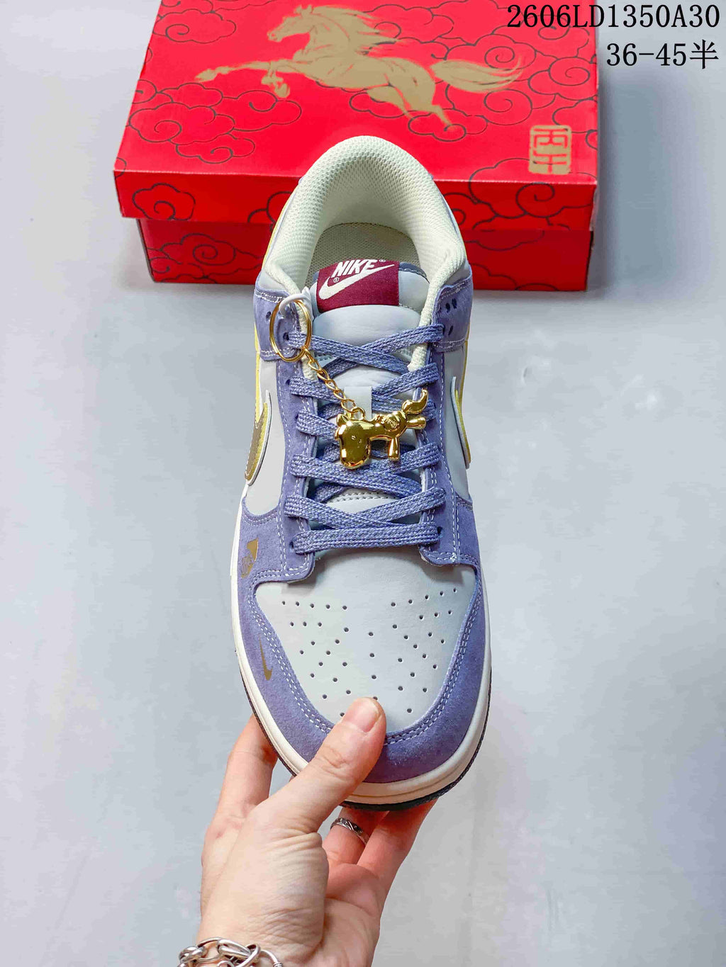 Front view of the Nike SB Dunk Low showing the perforated toe, lavender overlays, and dangling gold-tone charm.