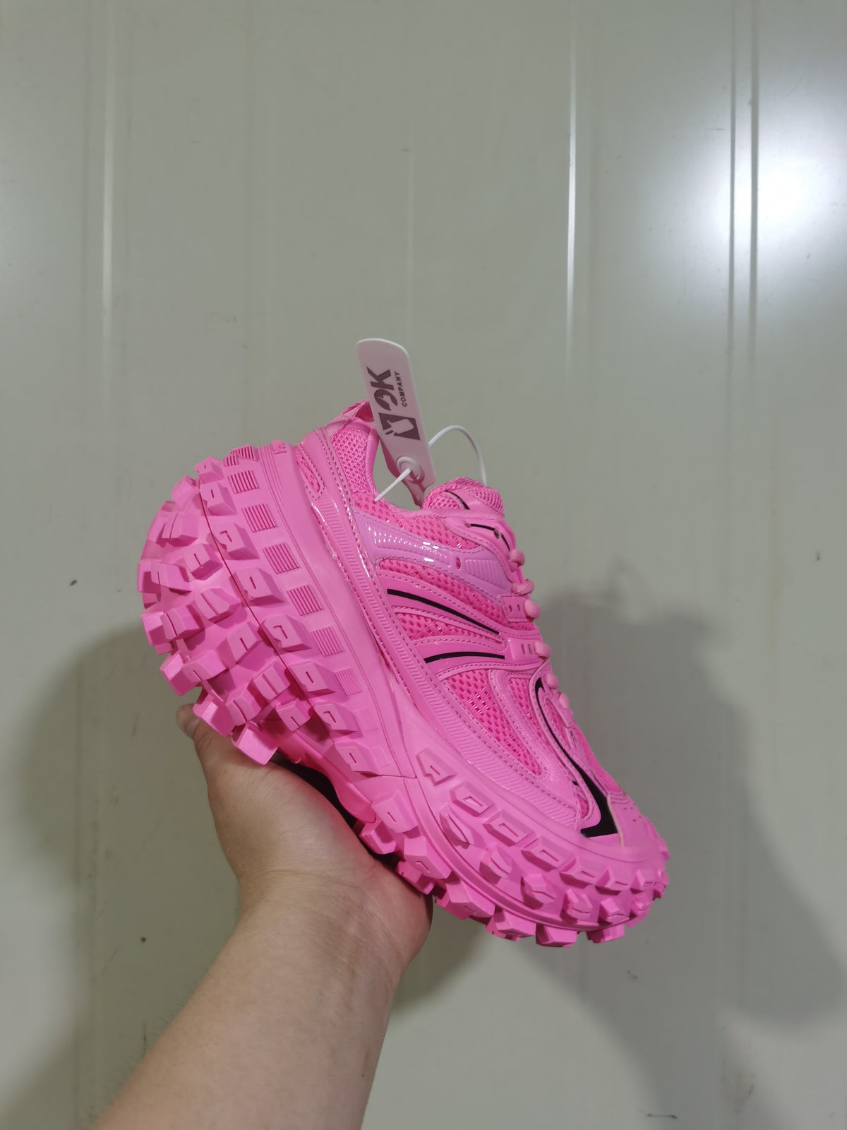 Side and top view of a bright pink lace-up sneaker held by hand, highlighting the mesh panels and deep outsole tread.