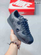 Close-up side view of a black Nike Classic Cortez sneaker showing the Swoosh, laces, padded collar and outsole; overlay text shows style code 2607JDY956A26 and size range 36–45.5.